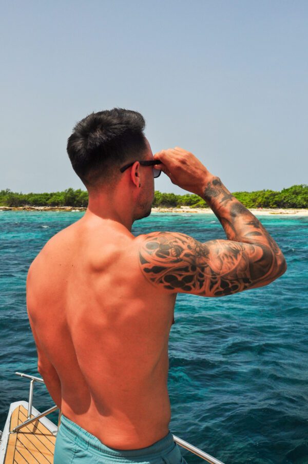 A man with tattoos on his arms looking out at the ocean.